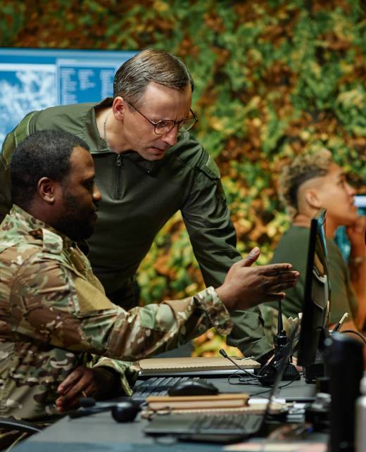 Young African American military officer in camouflage uniform pointing at computer screen while explaining graphic data to colleague